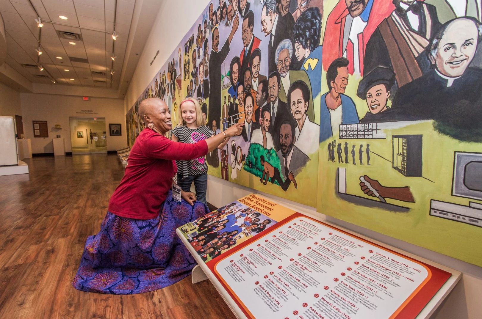 Tubman African American Museum an adult bends down next to a child, pointing out something on a mural