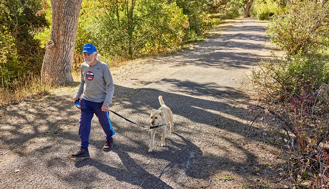 A senior man walks his dog along a gravel trail