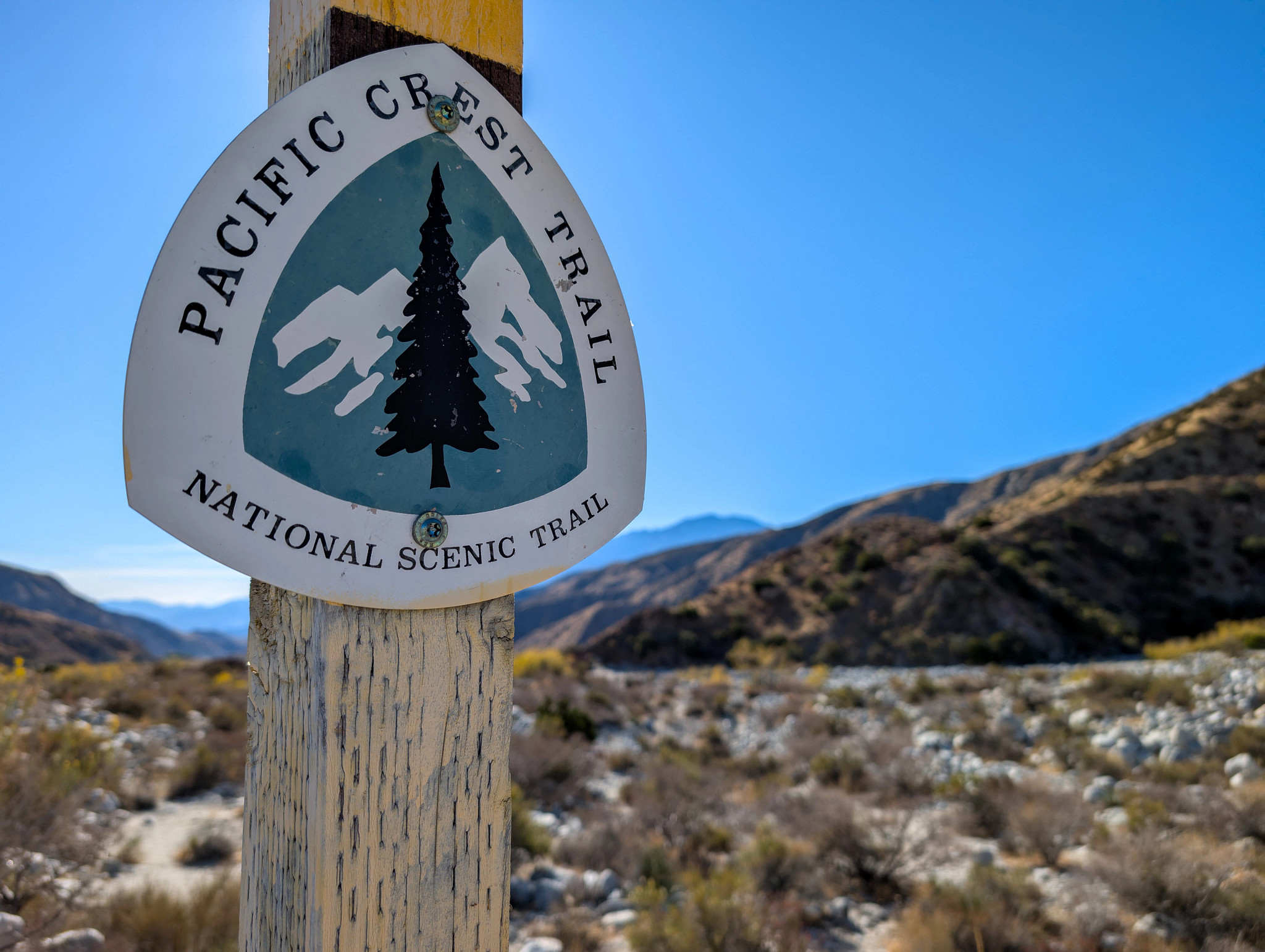 a Pacific Crest Trail sign with mountains in the background