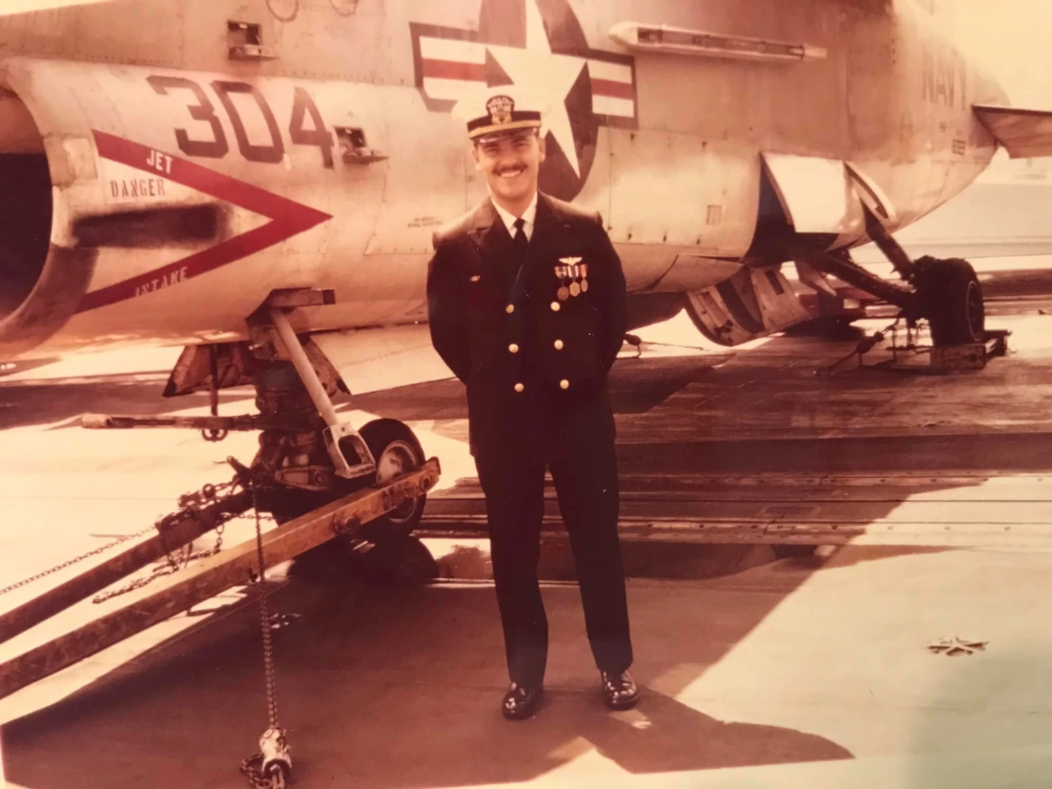 A sepia-toned photo shows the author’s father-in-law, Jim Lichtenwalter, smiling as he stands in front of his Corsair A-7 attack jet