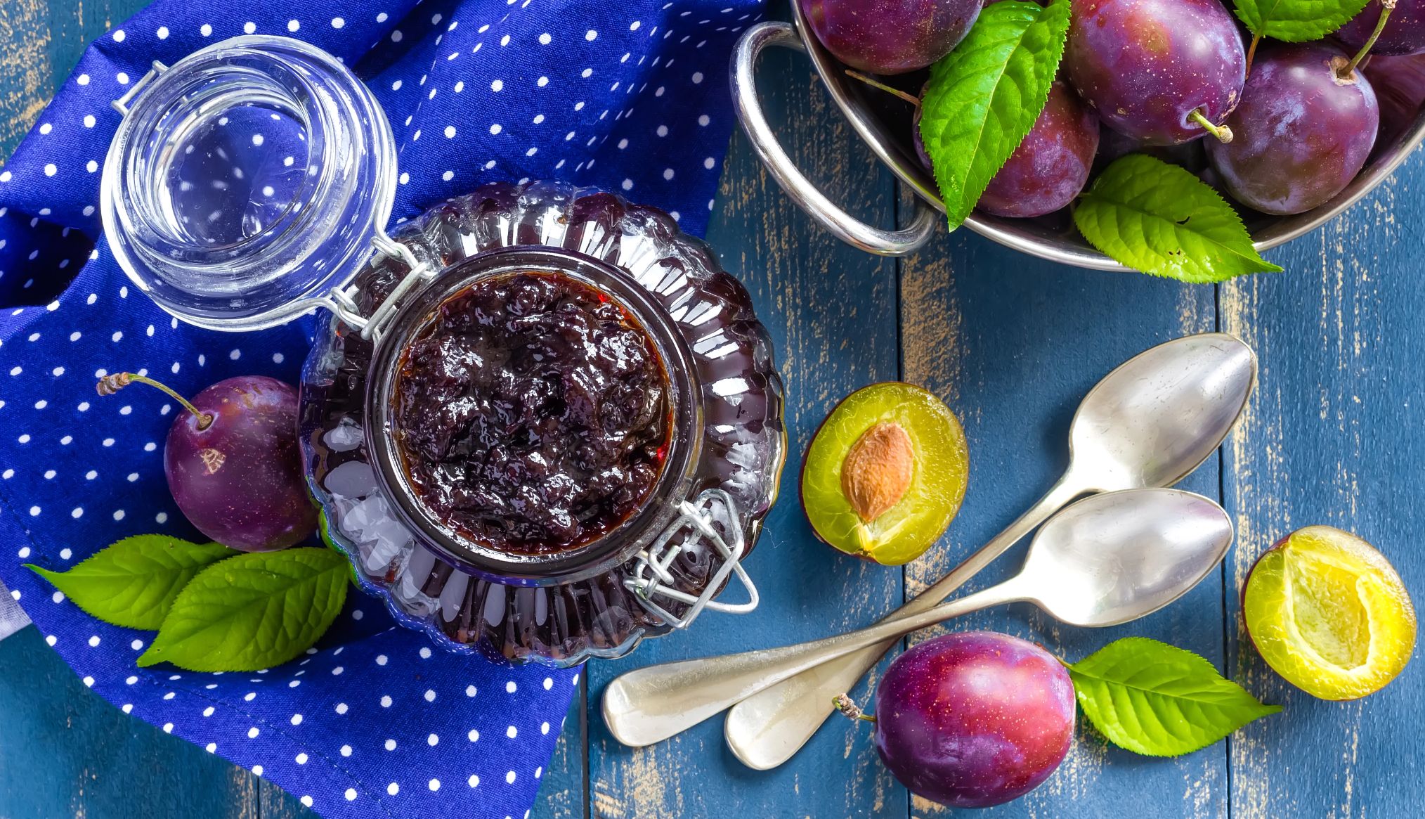 a jar of jam next to fresh prunes on a blue picnic table