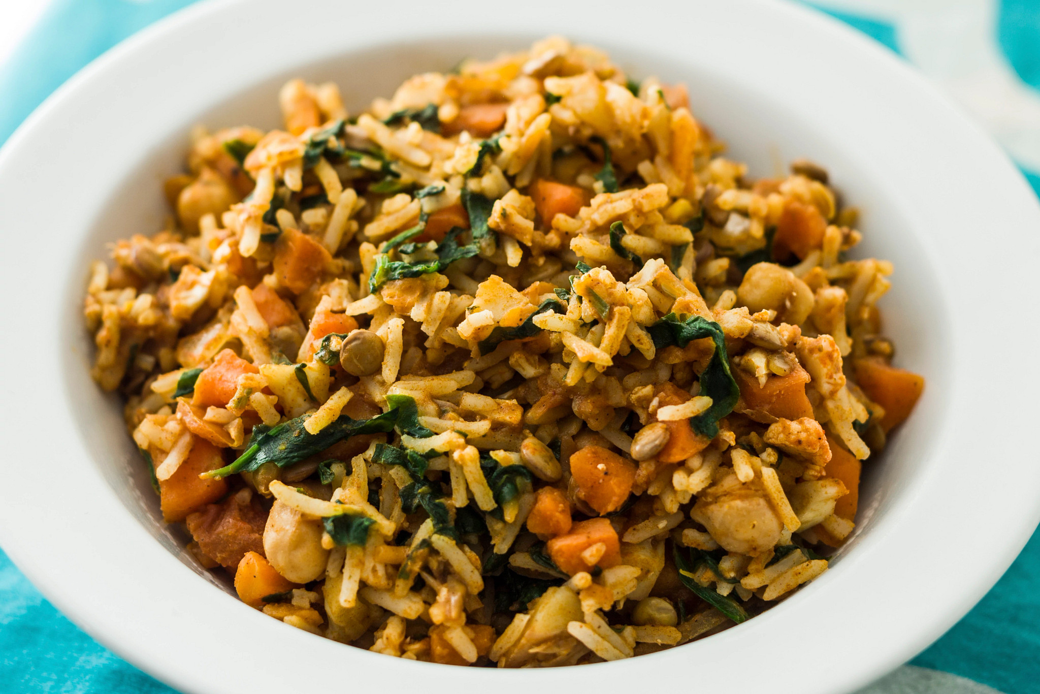 Close-up of a vegetable rice bowl featuring leafy greens, carrots, legumes, and seasoned rice in a white dish