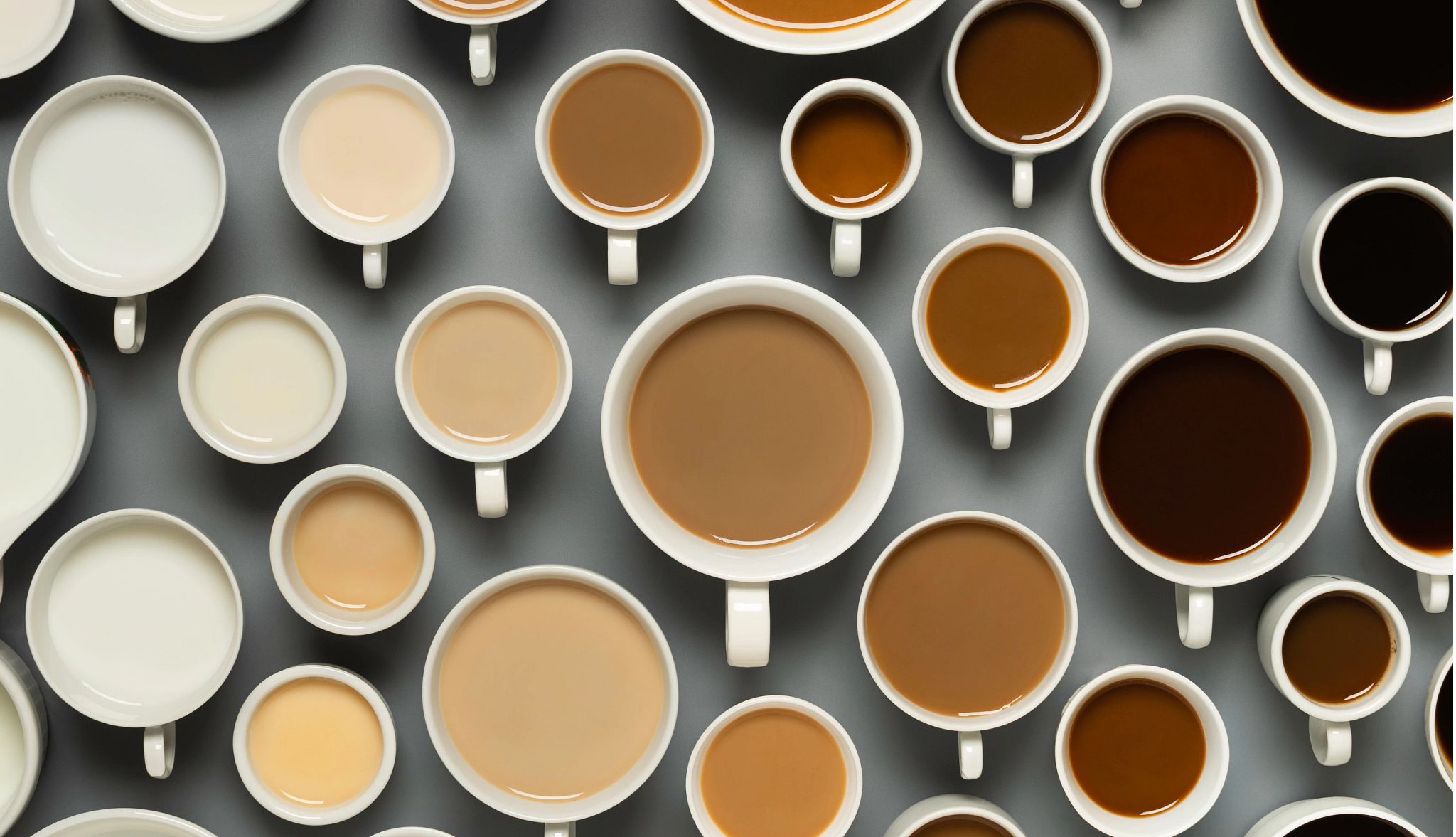 National Coffee Day Deals a photograph shows an overhead view of table filled with coffee cups of various sizes filled with coffee and milk