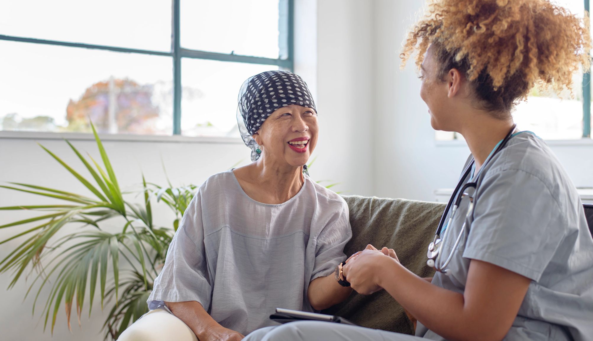 What to know about palliative care senior woman smiles while talking and sitting next to a nurse who is providing care