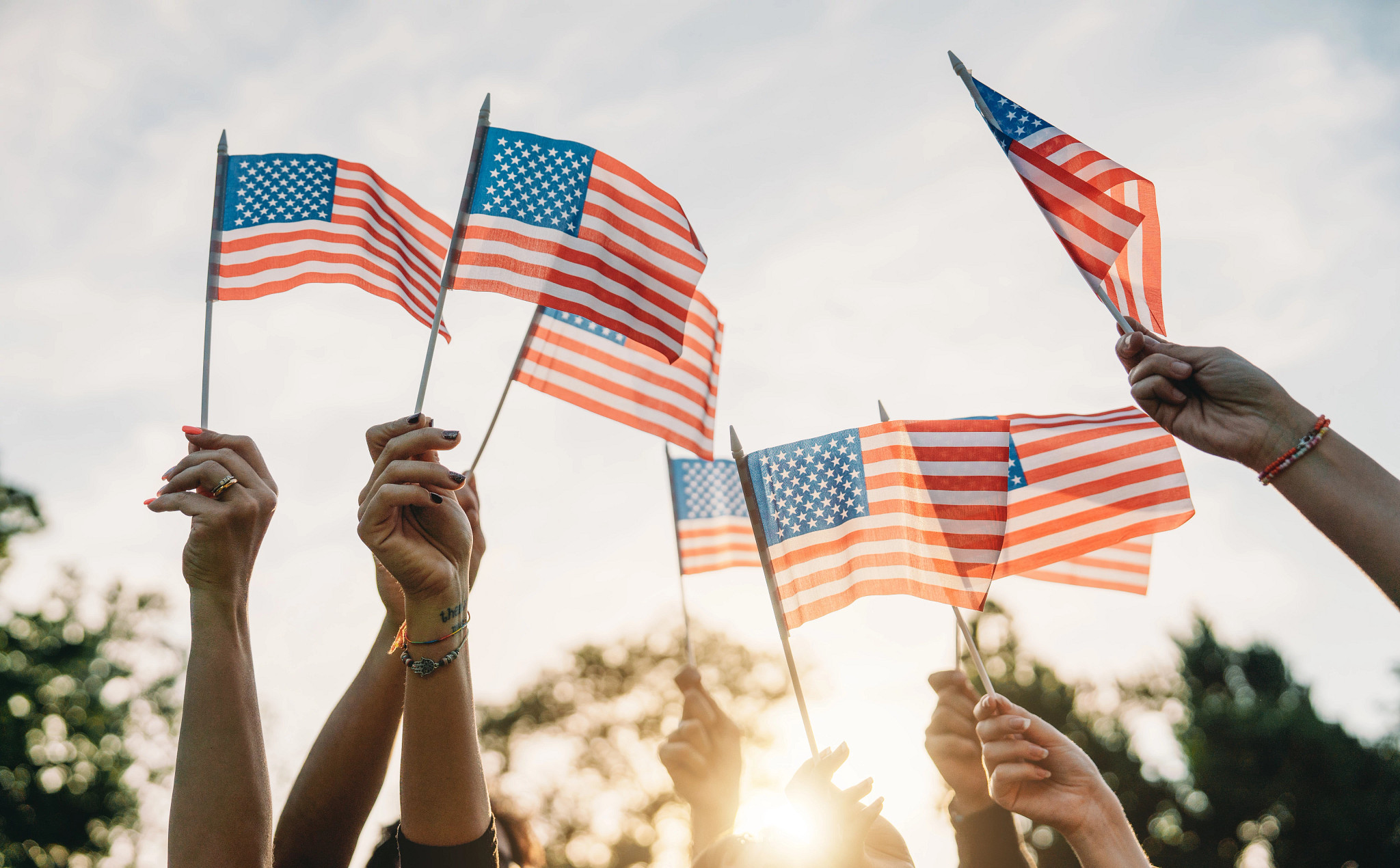 A group of people is waving small American flags at sunset.