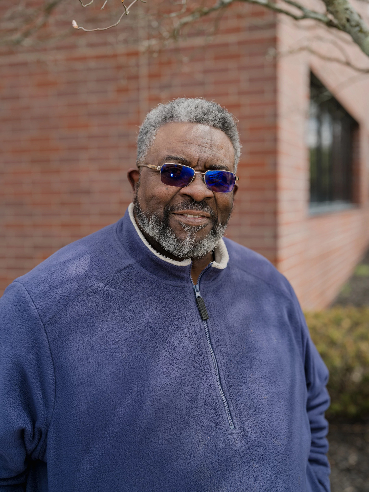 james rollins senior, wearing a dark blue pullover and sunglasses, stands outside a brick building