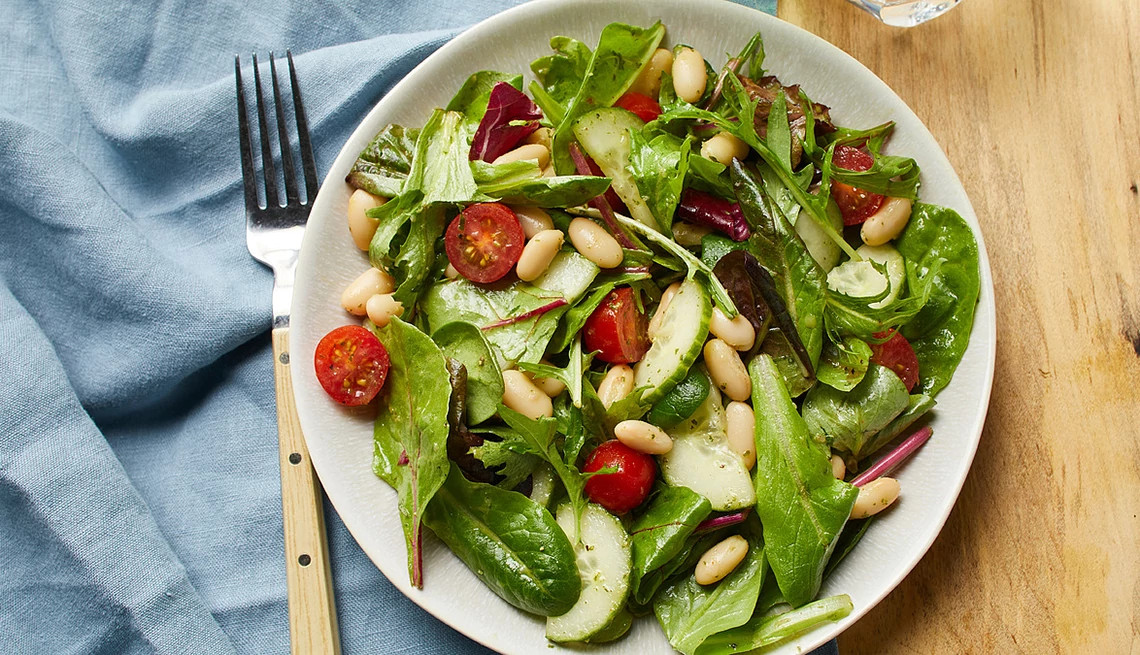 A close-up view of a tomato, cucumber and white bean salad with basil vinaigrette on a plate