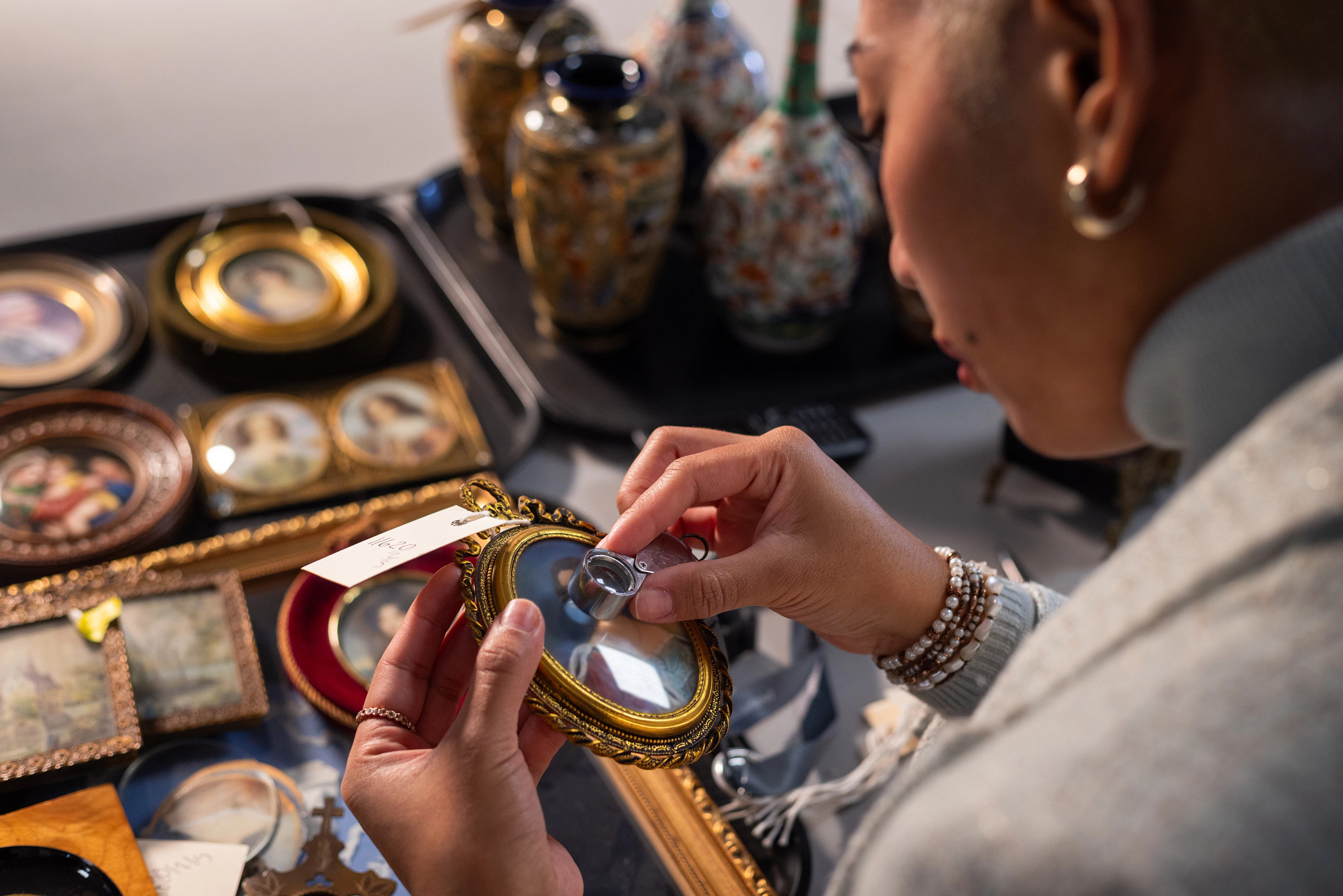 a photo shows a woman examining an antique with a small magnifying glass