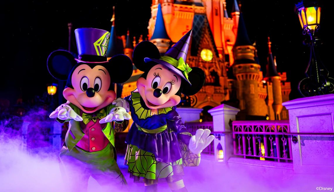 Walt Disney World Resort Mickey Mouse and Minnie Mouse dressed in Halloween costumes standing in front of Cinderella's castle decorated for Halloween at Walt Disney World