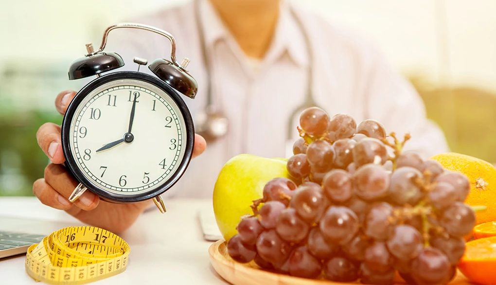 Note the times when you are most productive A person holding an alarm clock with fruits in front of him