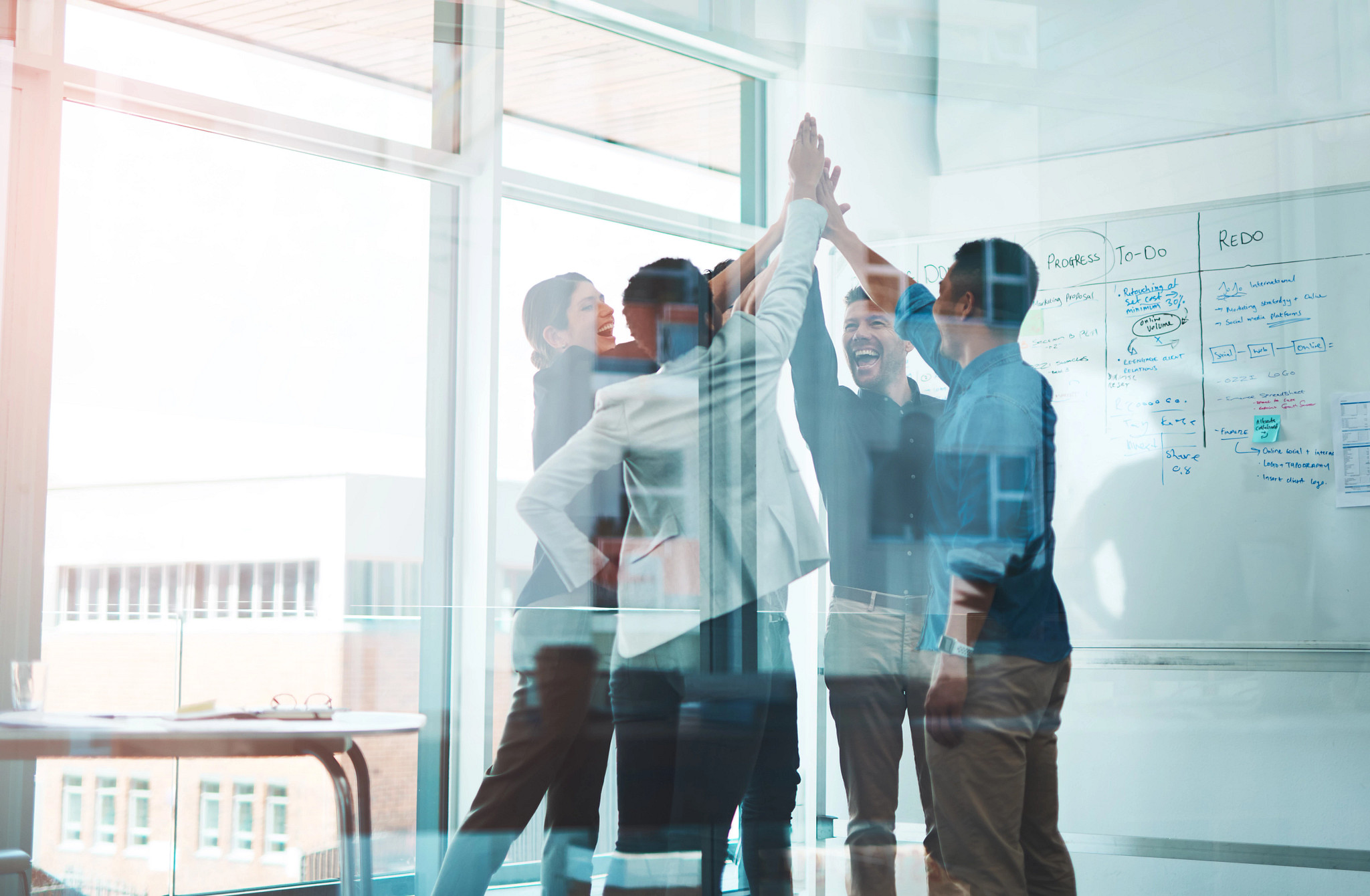  a group of coworkers in a meeting room high-fiving