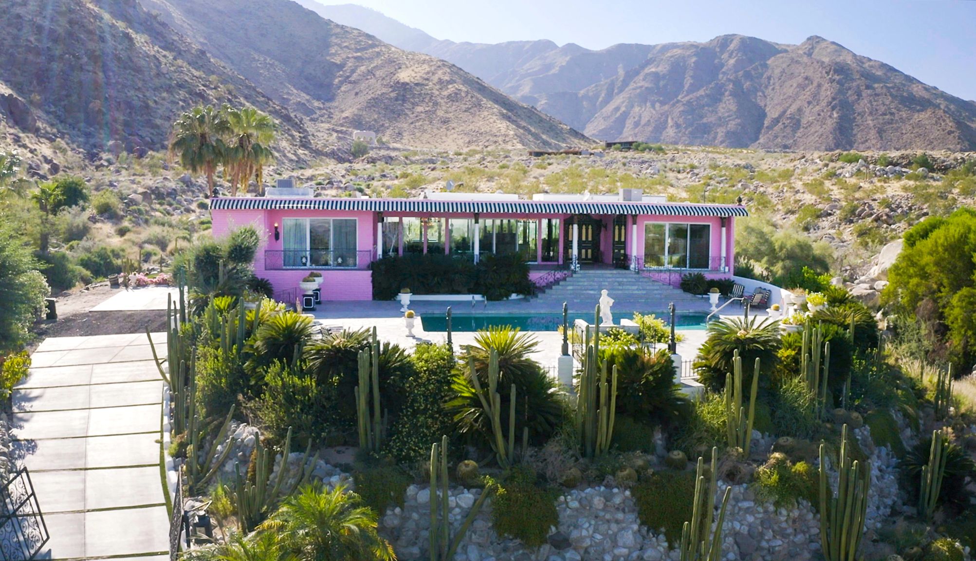 The 'Pink Palace' Pink house with shrubs in front and on the sides and mountains behind it