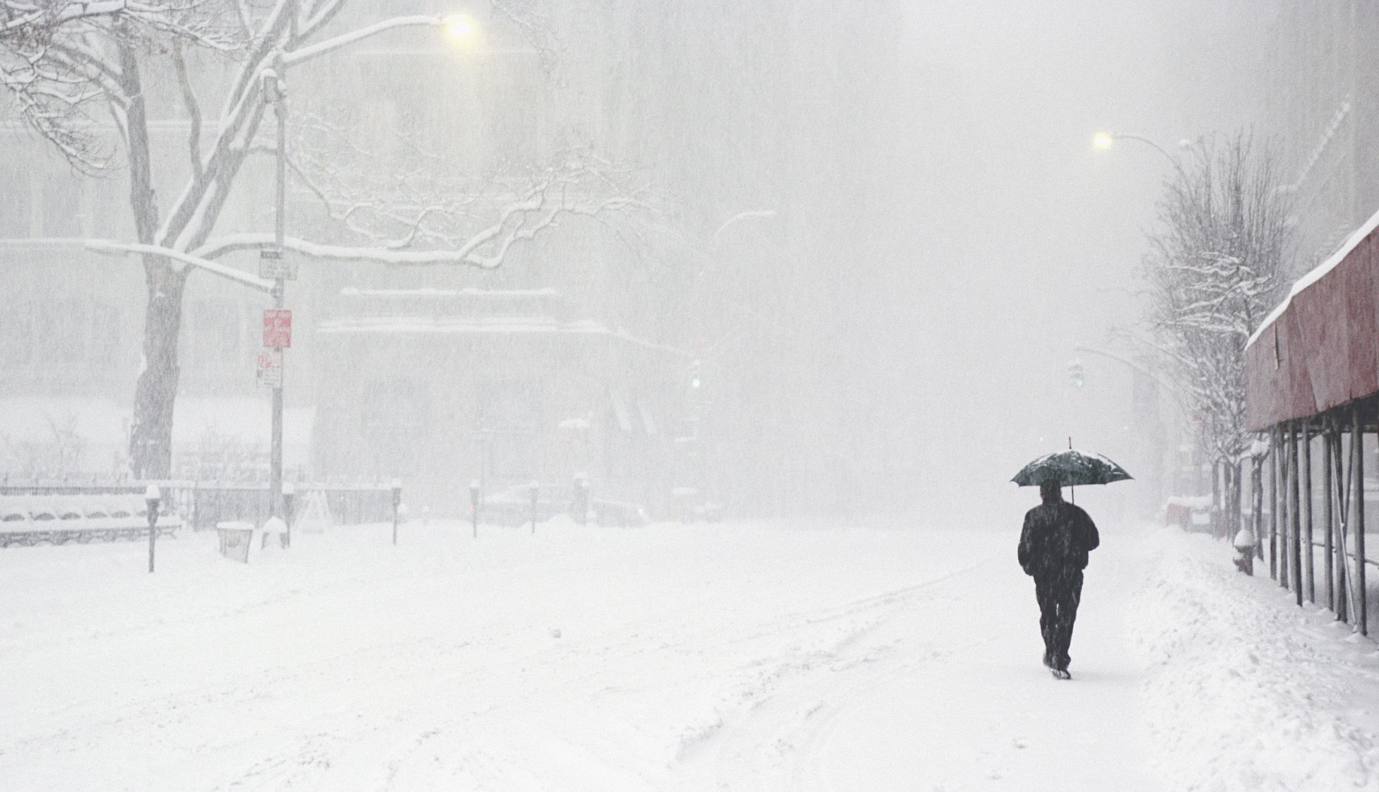 Un hombre vestido de negro bajo un paraguas camina por una calle en medio de una nevada.