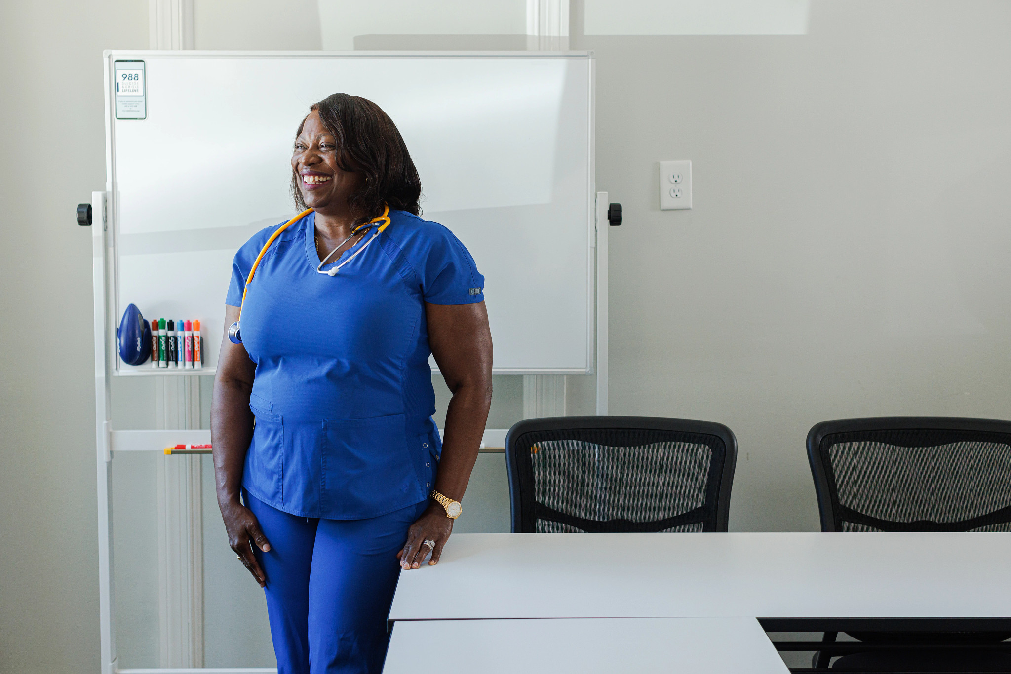 a woman wearing medical scrubs stands and smiles in an office