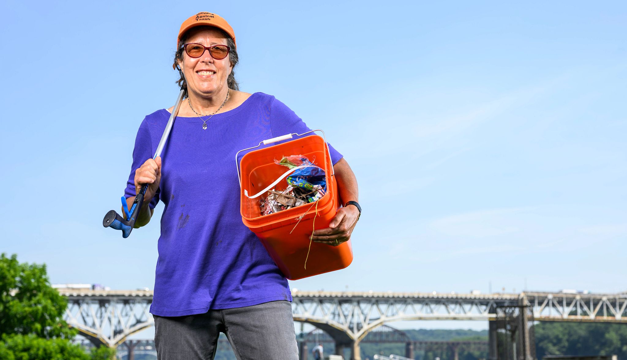 The Joy of Picking Up Trash A photo shows recent retiree Kim Clark picking up trash with a grabber tool and a plastic bin.