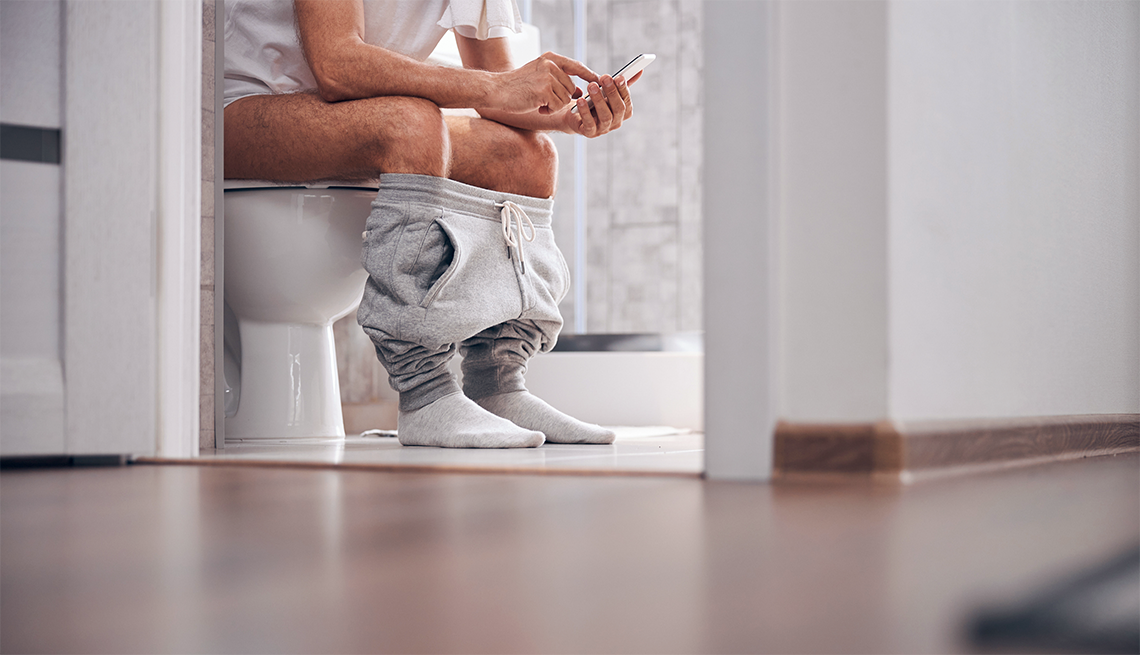a man sitting on a toilet reading his smart phone
