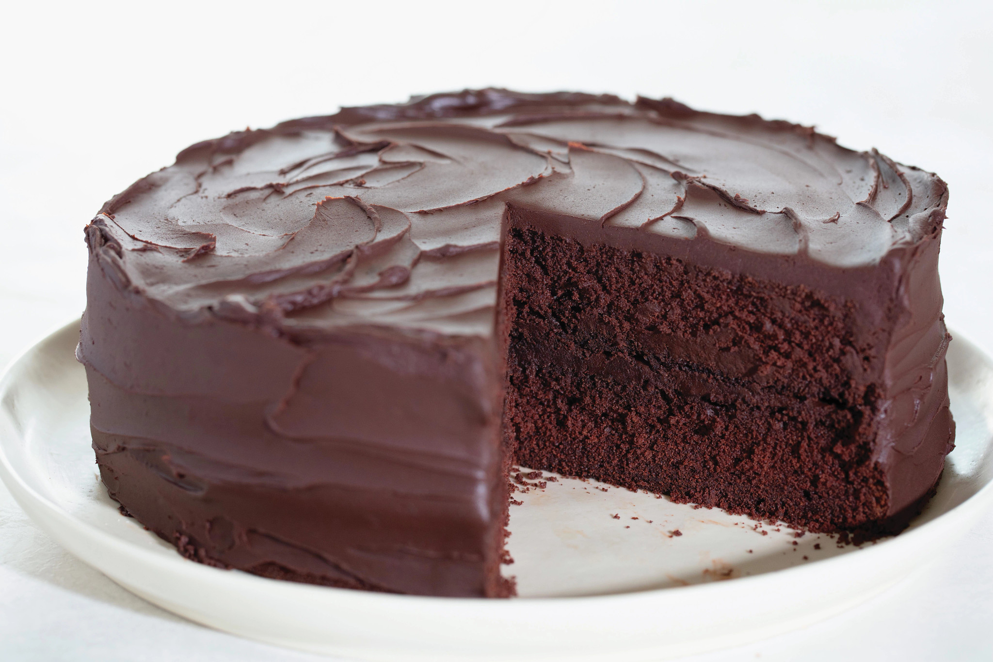 Chocolate cake with chocolate icing, with one piece cut out on dish