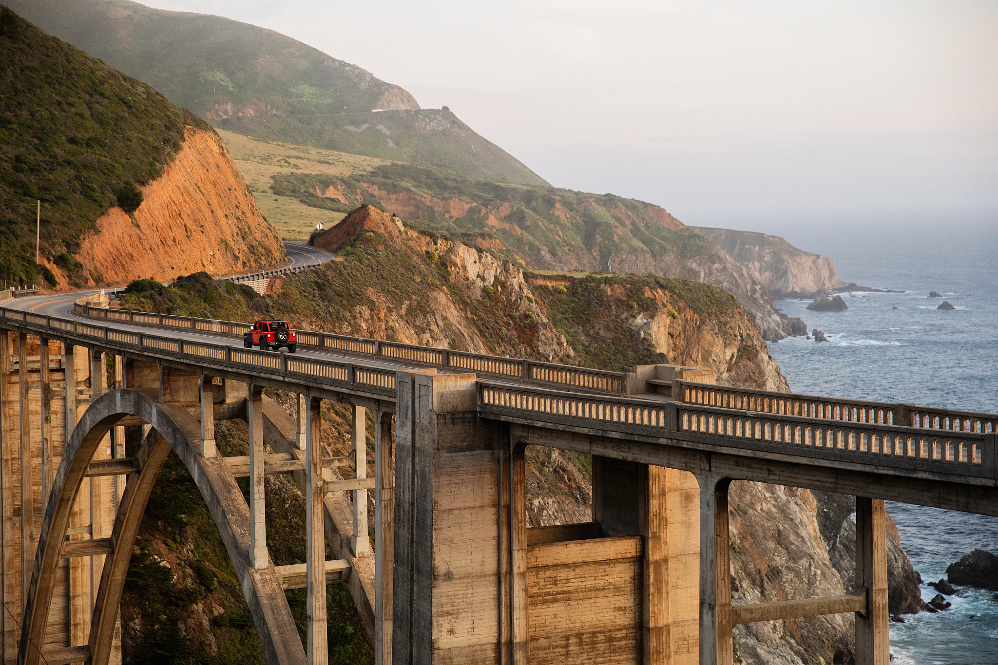 a red jeep drives along the famous Bixby Creek Bridge in Monterey County﻿