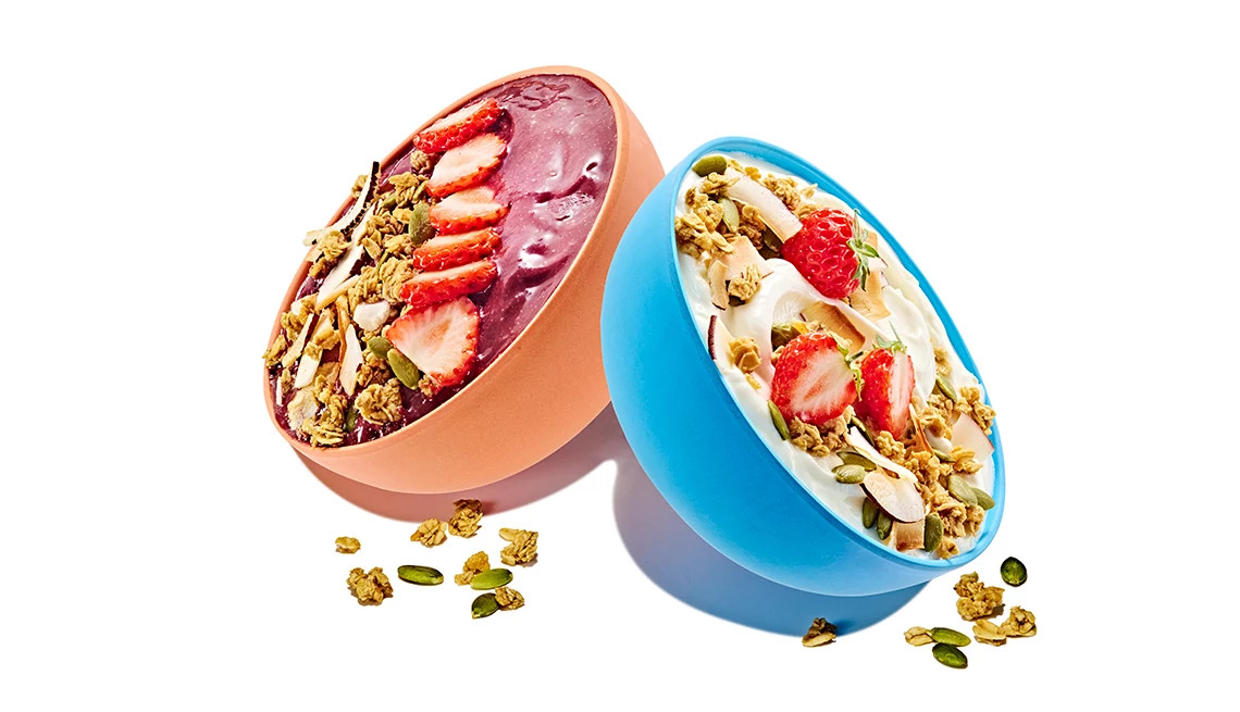 Two bowls angled to opposite sides; left bowl has acai, strawberries and granola; right bowl has yogurt, strawberries and granola