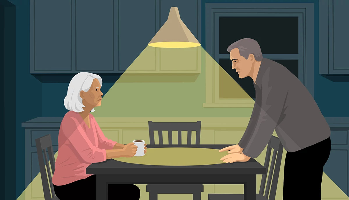 An illustration shows an older adult man confronting his wife, who is sitting at the kitchen table with a cup of coffee. He is standing at the other end, with both hands on the table