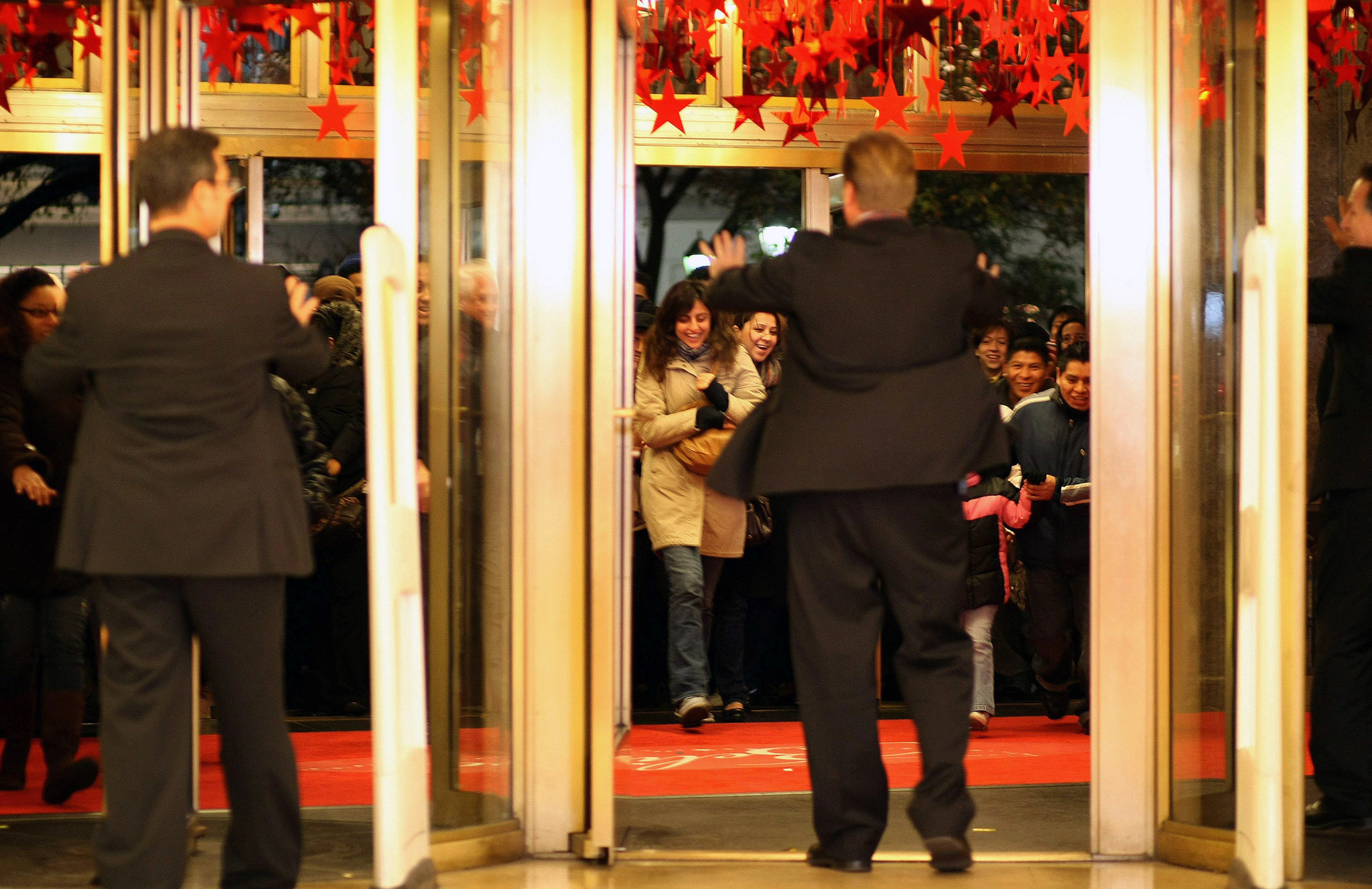 Dos guardias de seguridad en trajes negros intentan frenar a una multitud de compradores entrando a la tienda
