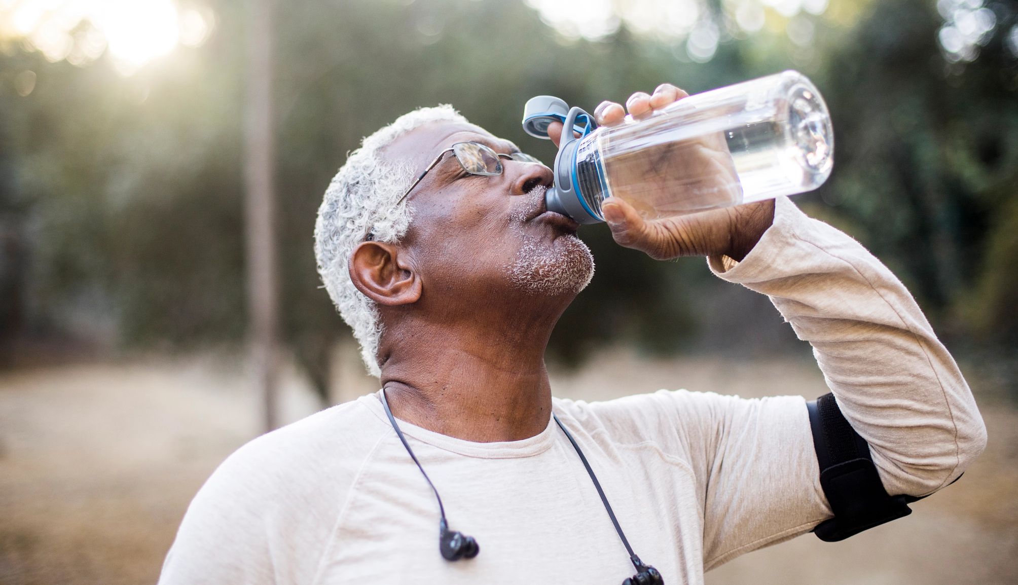 a man wearing headphones around his neck takes a drink from a clear plastic water bottle