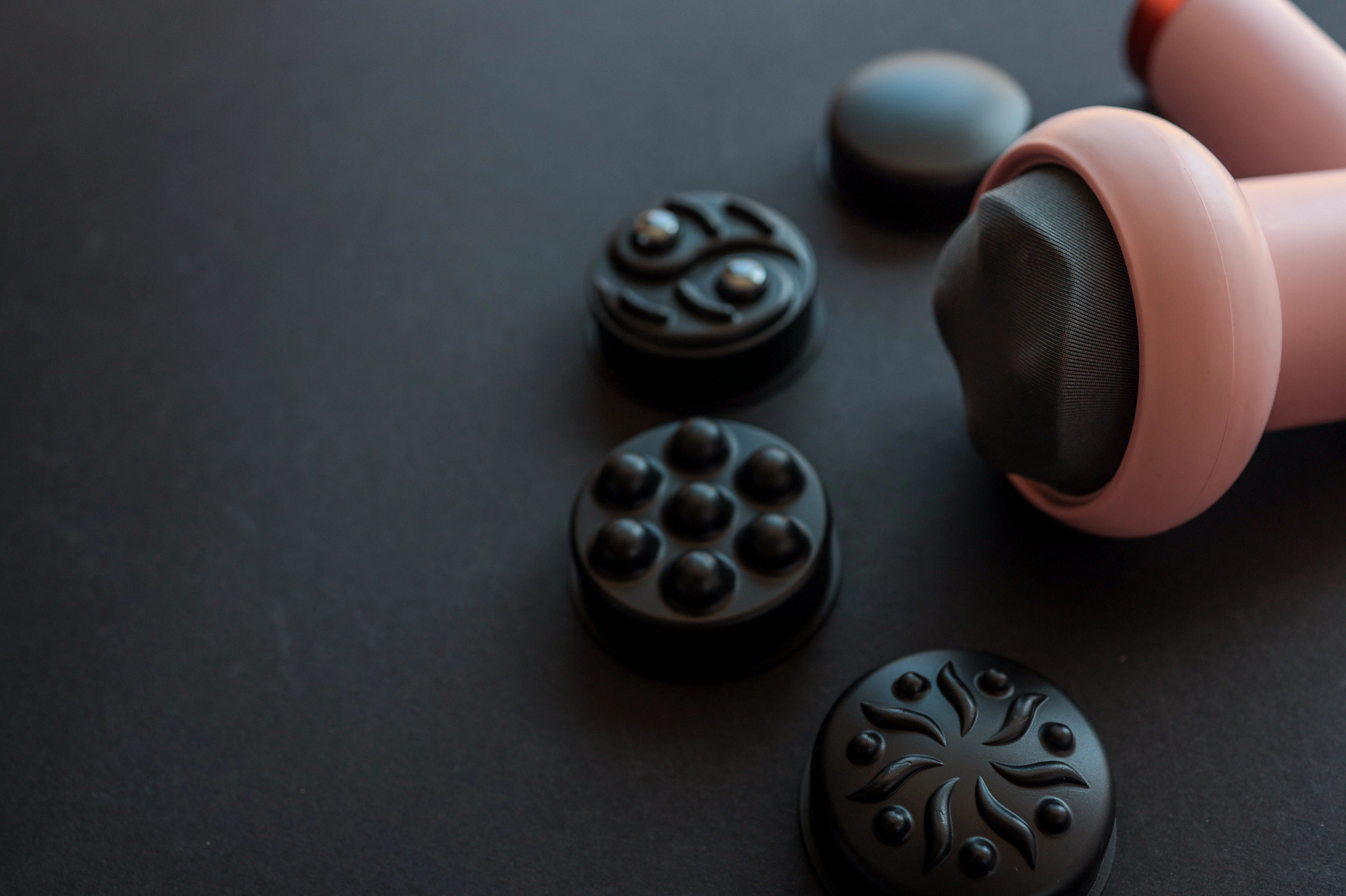 pink percussive massage tool with several different attachment heads on a black background.