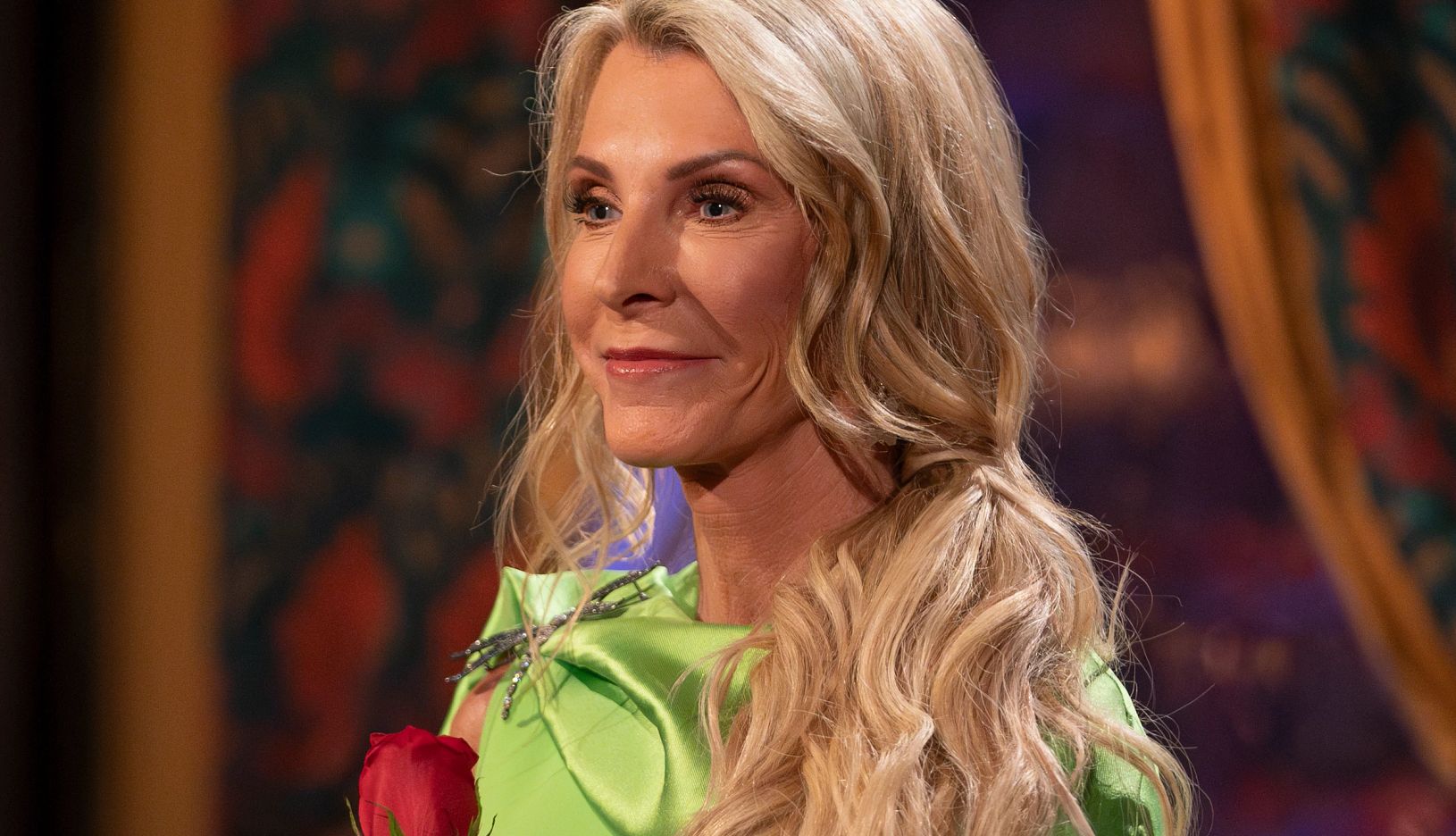 The Golden Bachelorette Joan Vassos wearing a green dress holds a red rose on The Golden Bachelorette