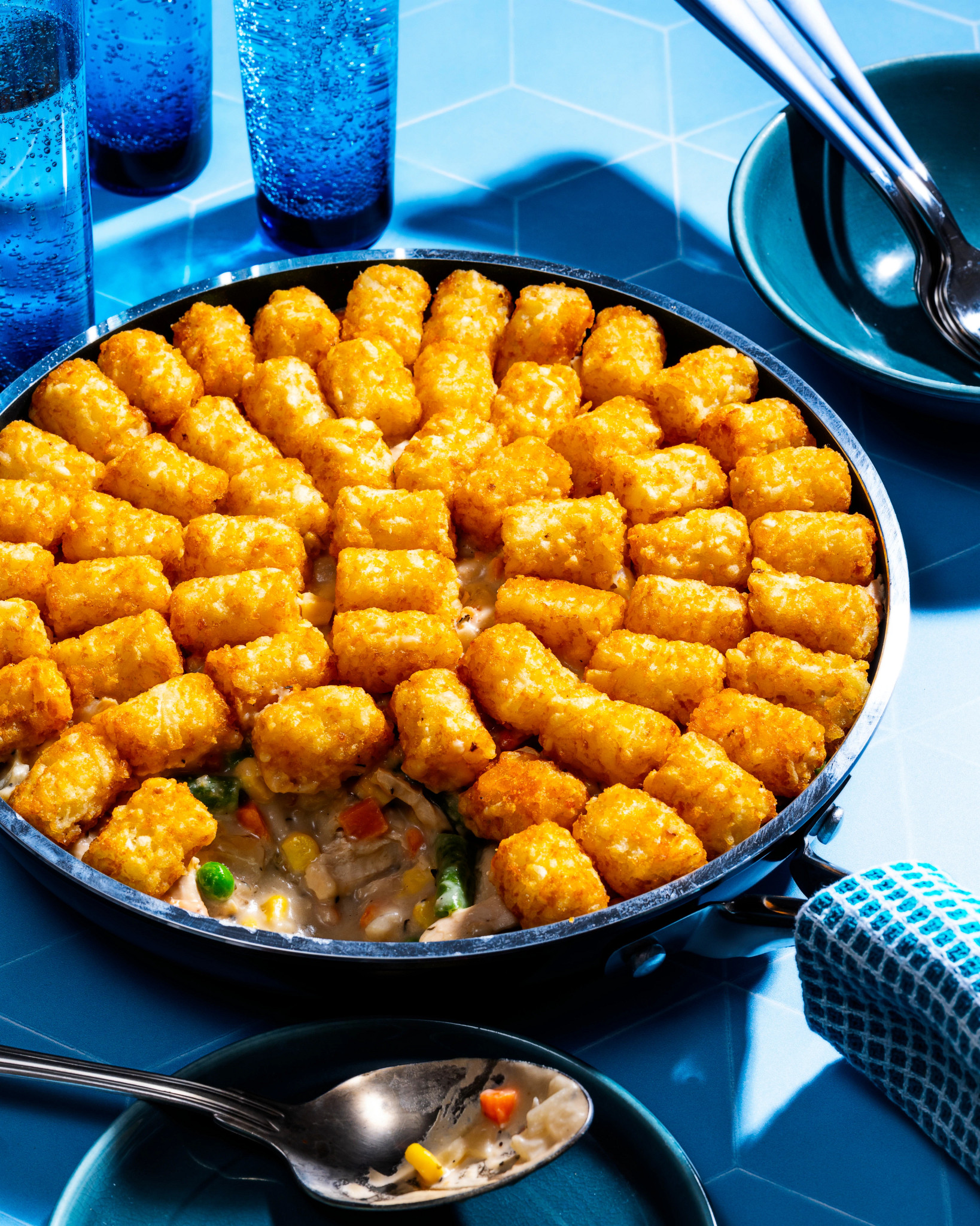 View of Tator Tot Chicken Casserole in a skillet on a blue background
