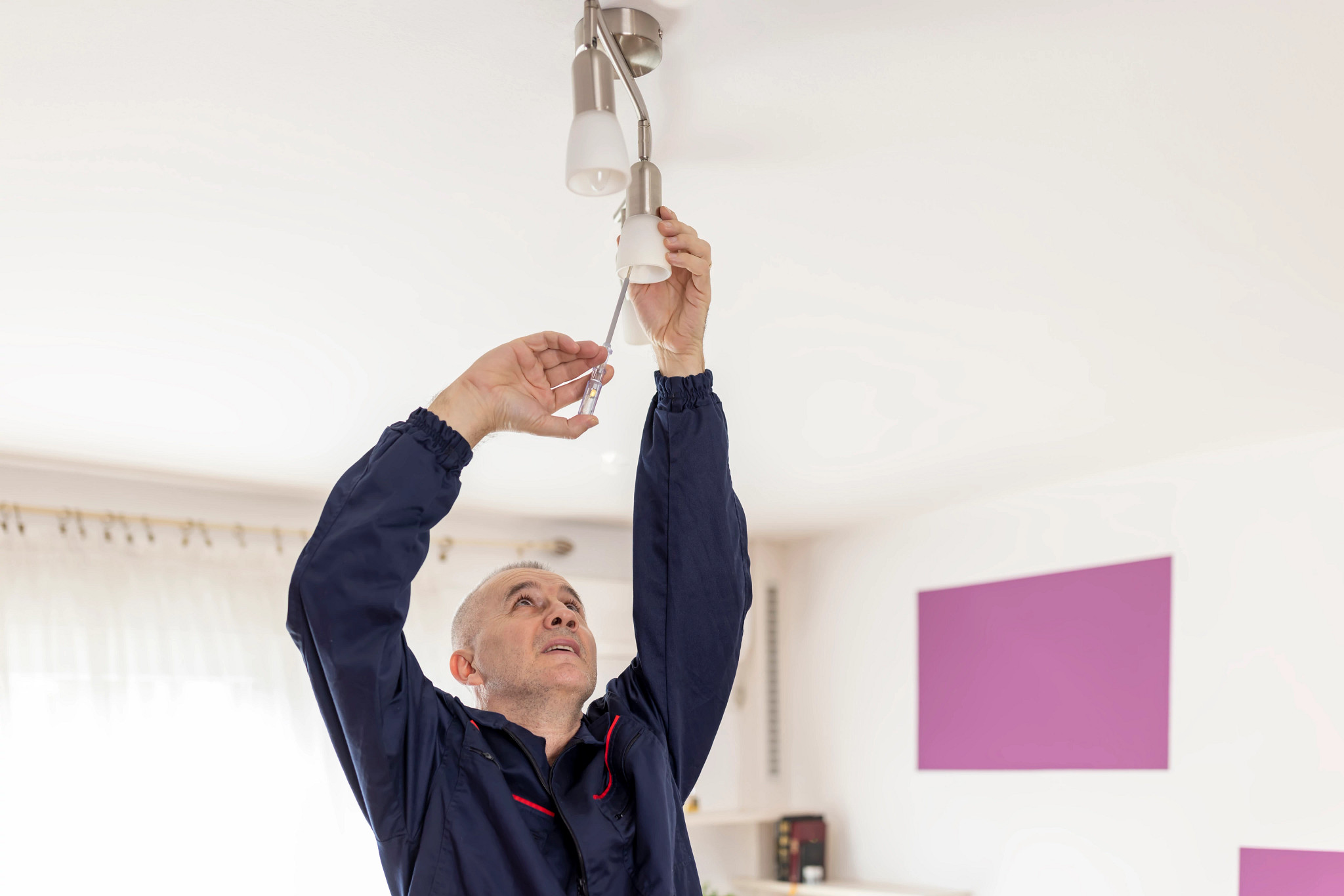 A photo shows an older adult male installing a modern-style light fixture in a home