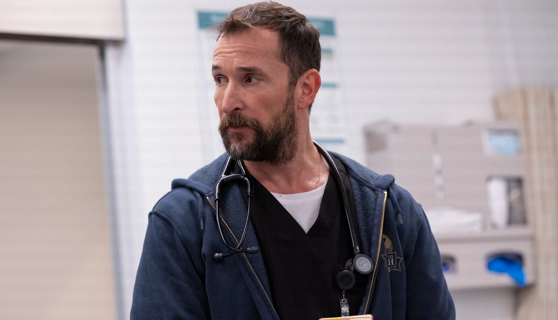 A scene featuring actor Noah Wyle in the medical drama series The Pitt Noah Wyle as Michael Robinavitch in The Pitt, wearing a dark blue jacket with a stethoscope and ID badge