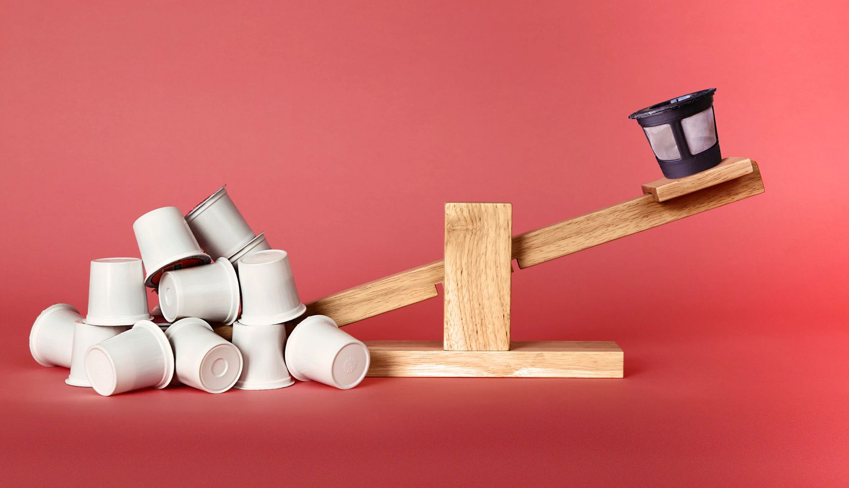 Save on Coffee Pods a seesaw with single use coffee pods on one end and a reusable coffee pod on the other