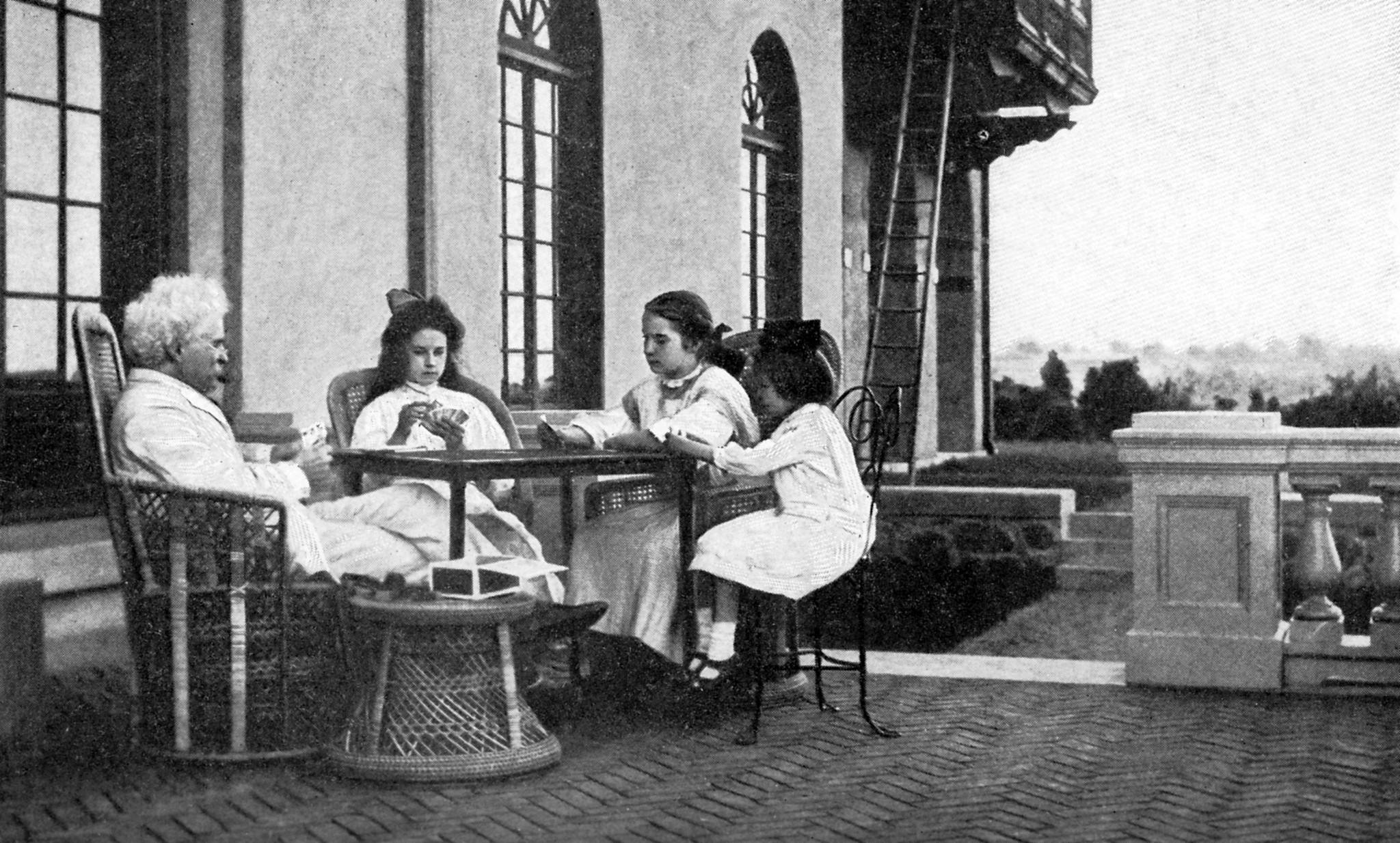Mark Twain, playing cards at an outdoor table with three young girls in white dresses