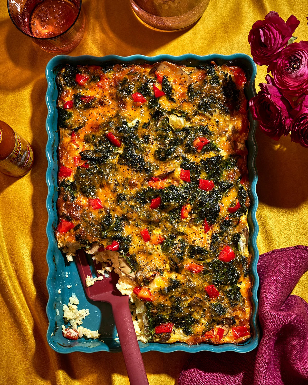 Spinach and red pepper casserole baked in a turquoise dish with a serving spoon