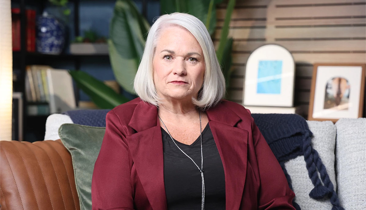 Janilyn Layton, dressed in a black shirt and dark red blazer, looks at the camera.