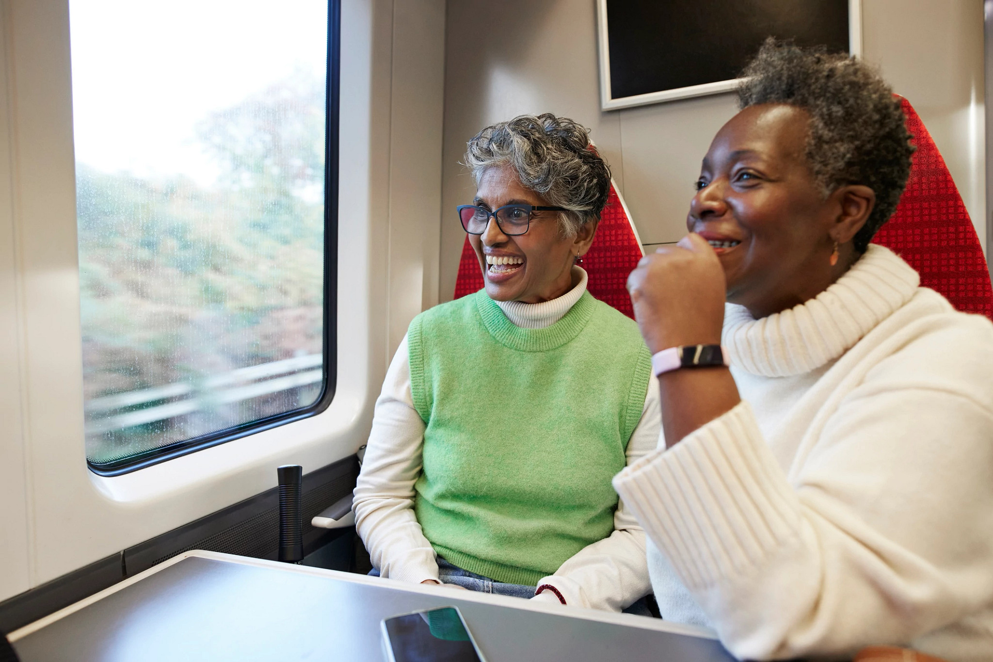 Happy senior female friends looking through window while traveling together in train