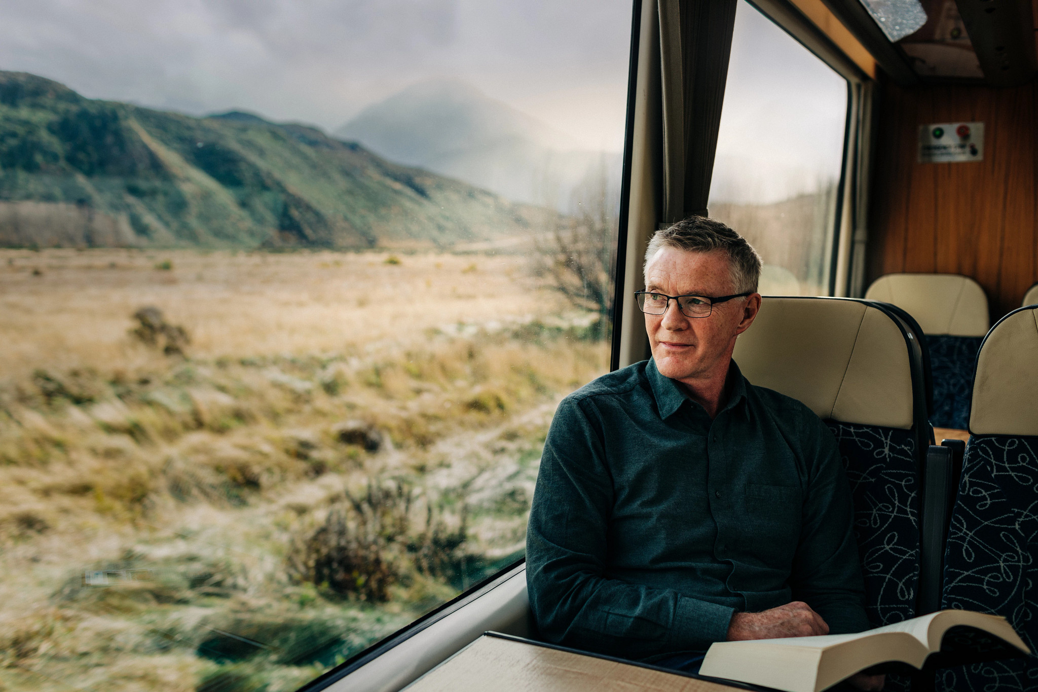 a man sitting in a train car with a book while looking out the window
