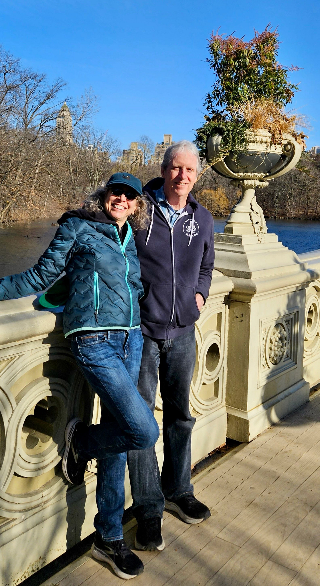 Laura Sturza and her husband Tom standing together on a bridge in Central Park with water and trees in the background