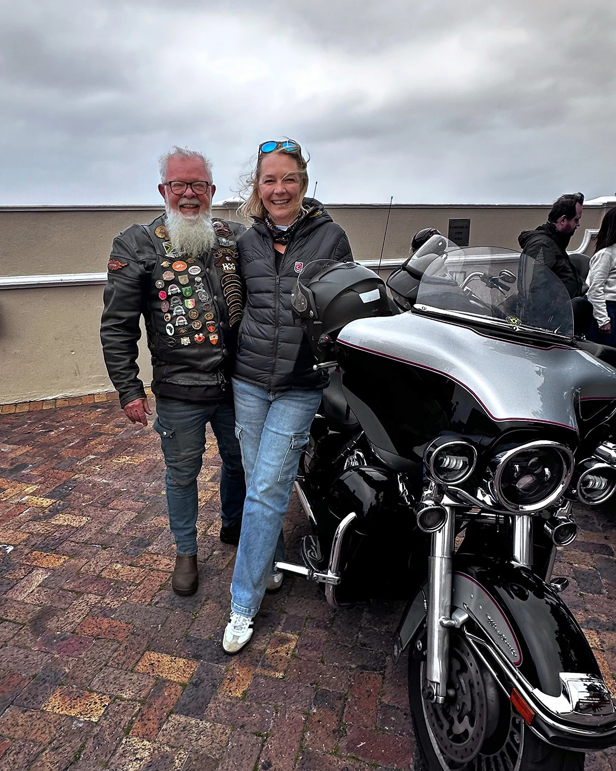 Woman and man with long beard smiling beside a motorcycle