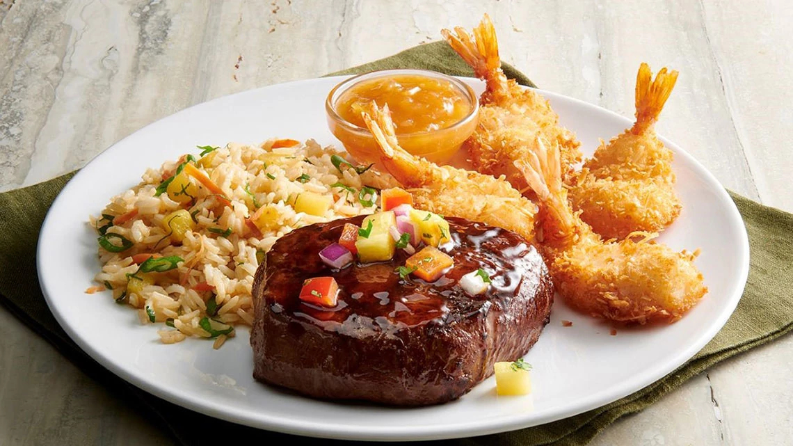 Rainforest Cafe White dinner plate with steak shrimp rice and sauce on green napkin wood table