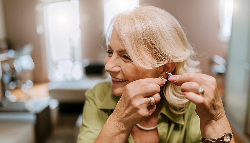 Hearing aids may slow cognitive decline A smiling woman putting a hearing aid in her ear