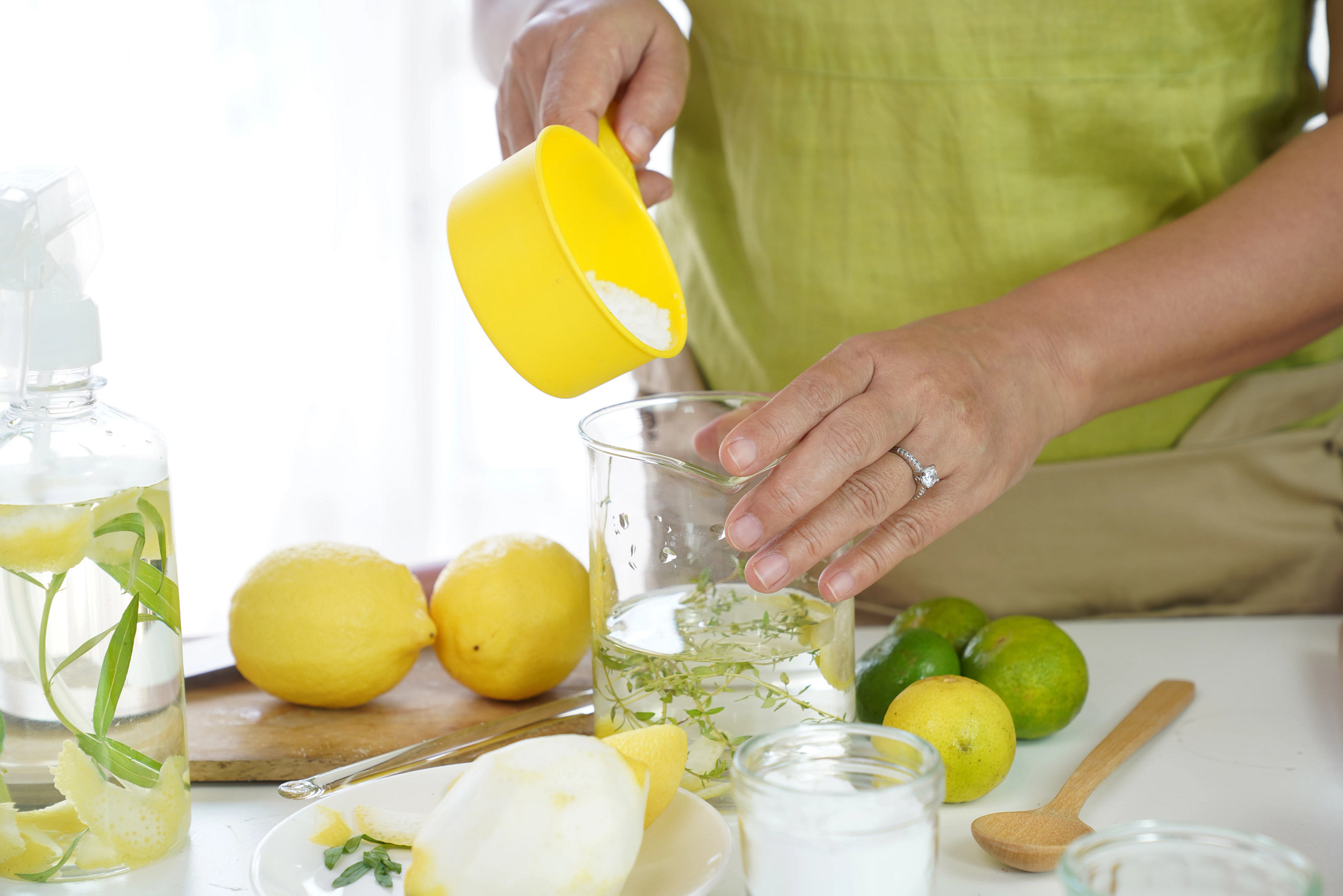 a photo shows a woman mixing baking soda into glass filled with herbs and liquid. There are lemons and limes on the counter