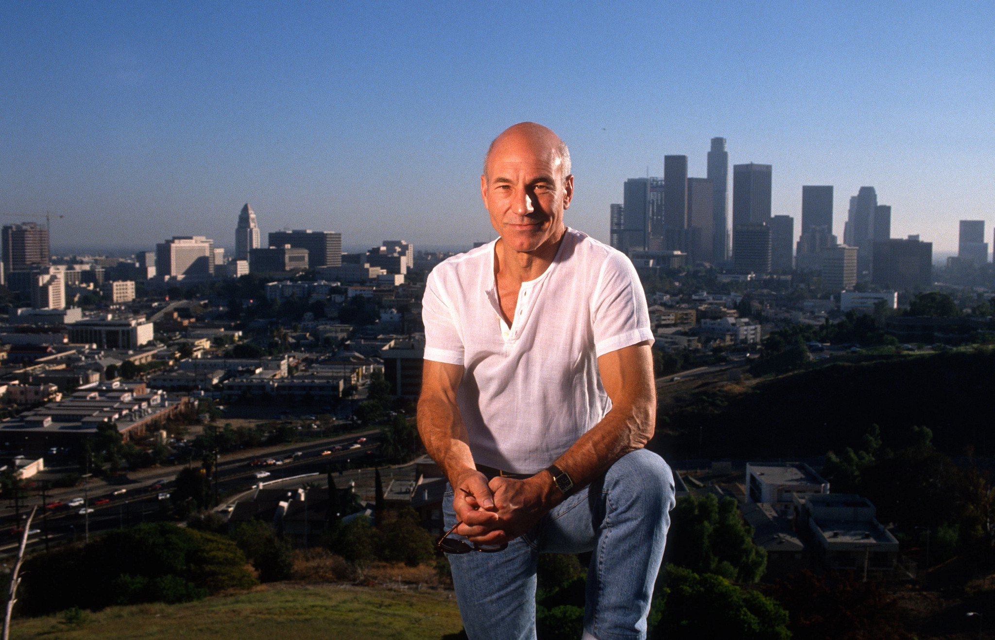 patrick stewart in a white shirt with the city of los angeles in the background