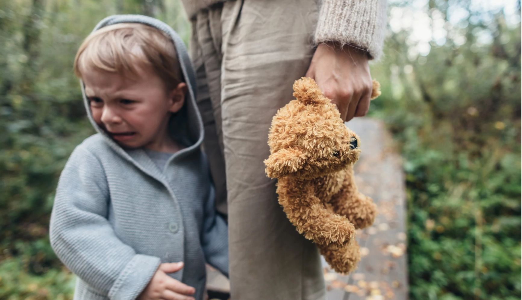 gentle parenting a chid cries while holding the hand of an adult whose also holding a teddy bear