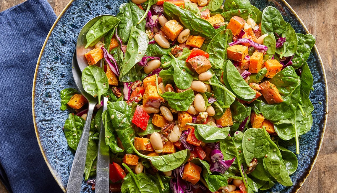 A close-up view of a spinach salad with roasted sweet potatoes, white beans and basil vinaigrette on a plate