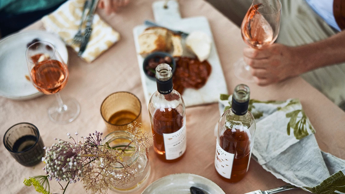 naked wines bottles open with glasses on table and plates with bits of food such as cheese, meat, crackers