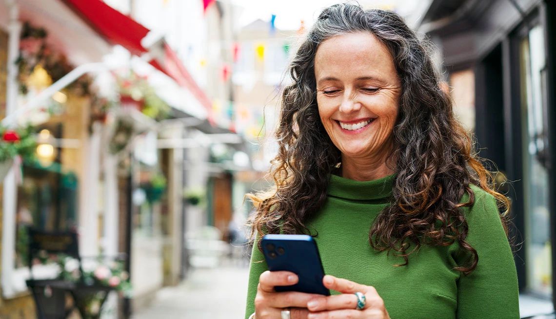 Member Benefits Text Alerts Woman in green sweater smiling while looking at phone while out walking on the street