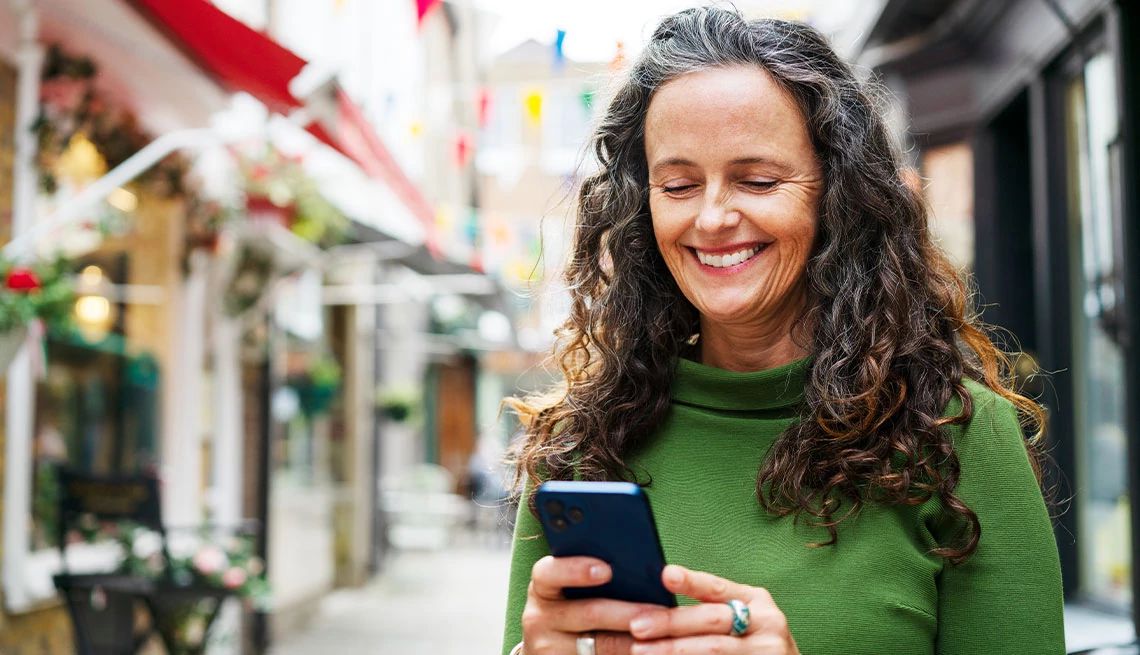 Woman in green sweater smiling while looking at phone while out walking on the street