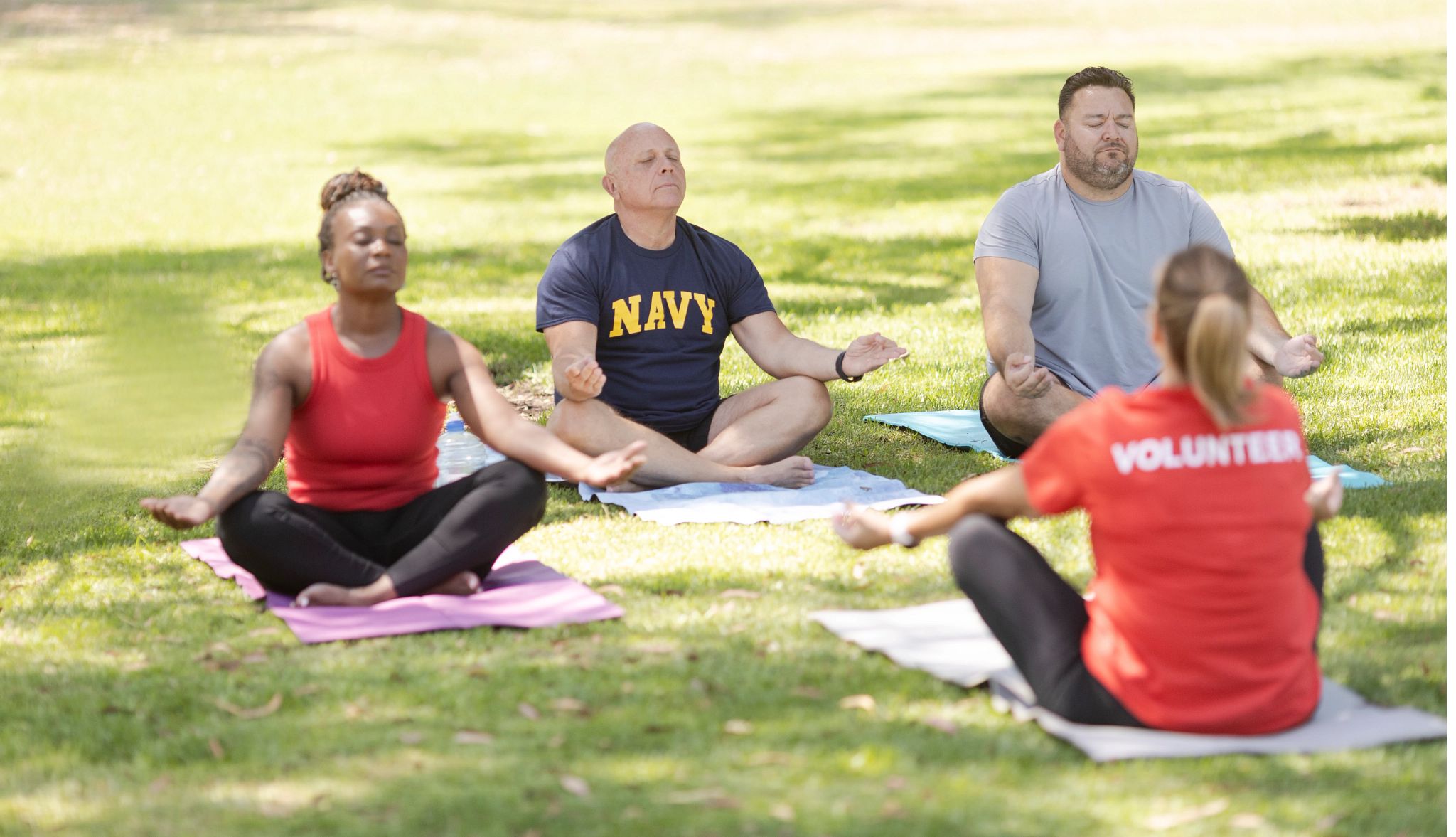A female volunteer leads a group of younger veterans outside in a meditation exercise outdoors in a park A female volunteer leads a group of younger veterans outside in a meditation exercise outdoors in a park