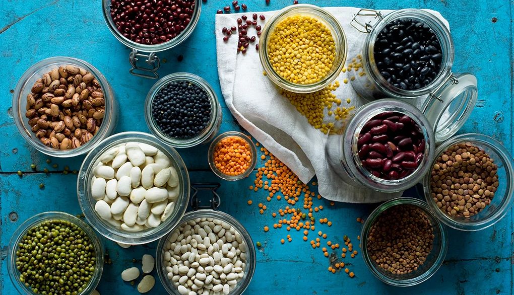 Regularly consuming beans and lentils may reduce the risk of heart disease and diabetes An overhead view of various beans and lentils in jars on blue background